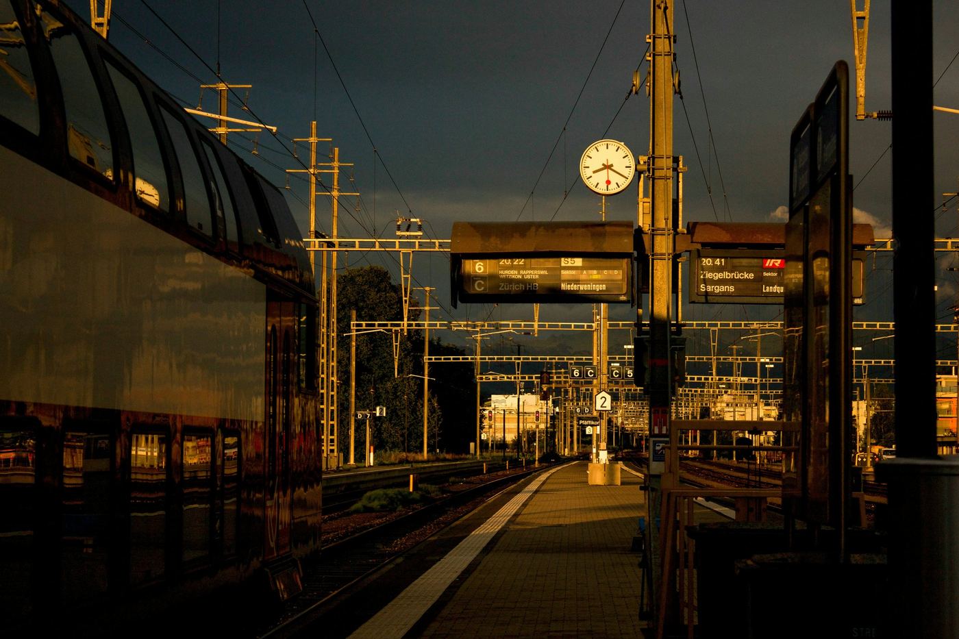 A station platform at golden hour, a clock against a dark sky