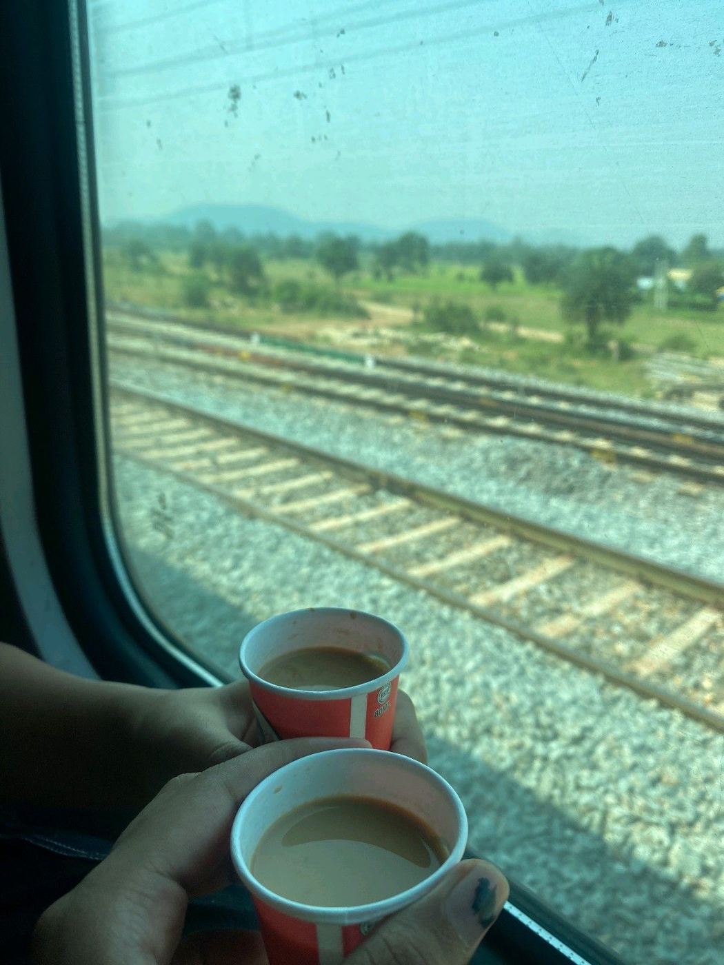 Two cups of chai held up to a train window