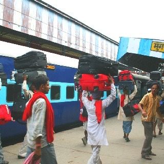 Coolies carrying luggage on their heads beside a blue train