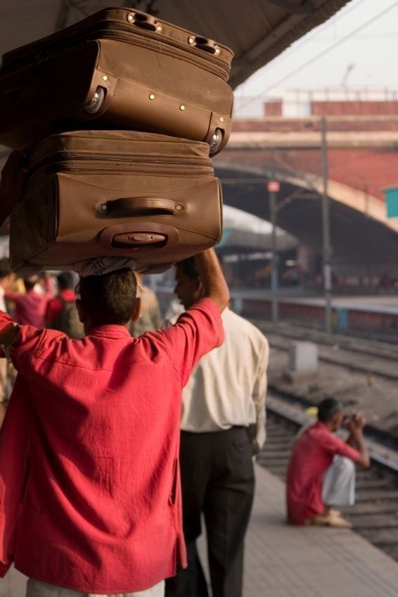 A coolie in a red shirt carrying two suitcases on his head